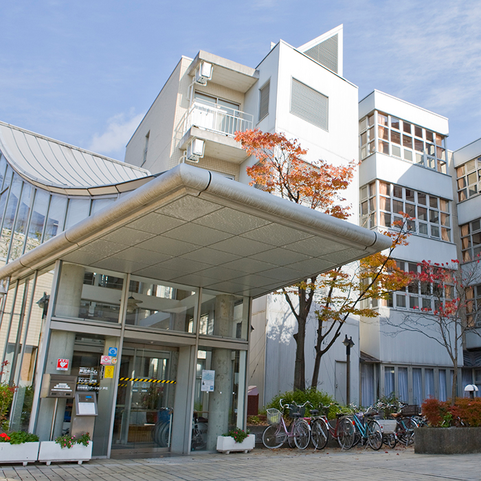 モダンな施設の玄関・車寄せ。キャノピー付きの広々とした入口に秋の樹木が見える。