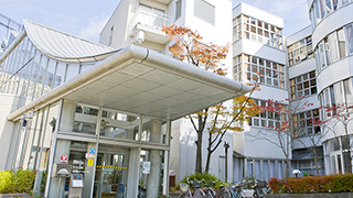 施設の外観と玄関周辺。モダンな建築デザインと周辺の街並み。